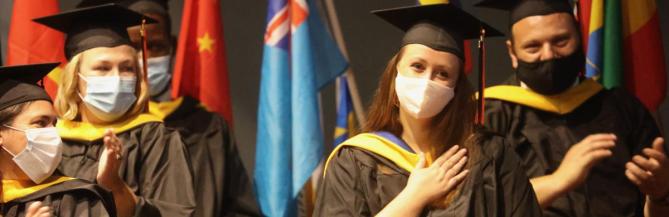woman in mask sitting in graduation garb